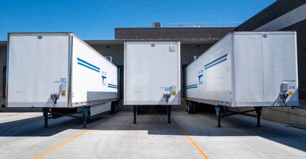 Three white cargo trailers parked at an industrial shipping dock under clear blue skies.